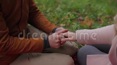 年轻夫妇坐在一个夏天的公园里，在一条格子的野餐毯上野餐。 公园里的一对